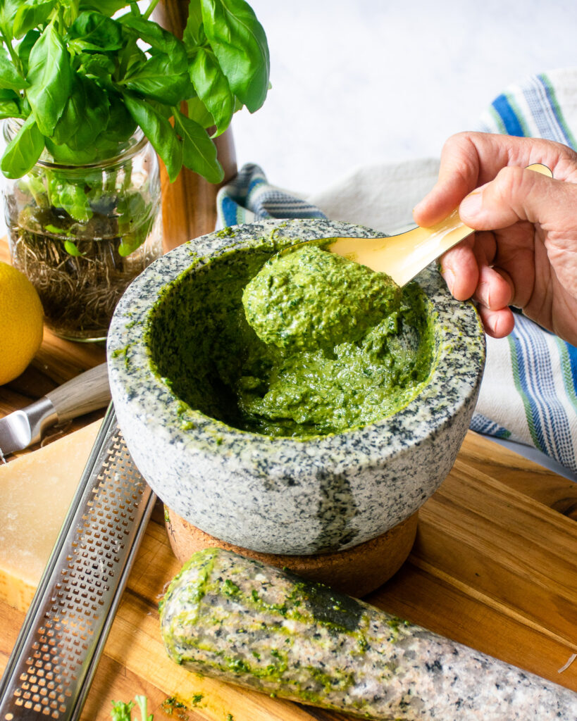 A spoonful of basil pesto being lifted out of a stone mortar.