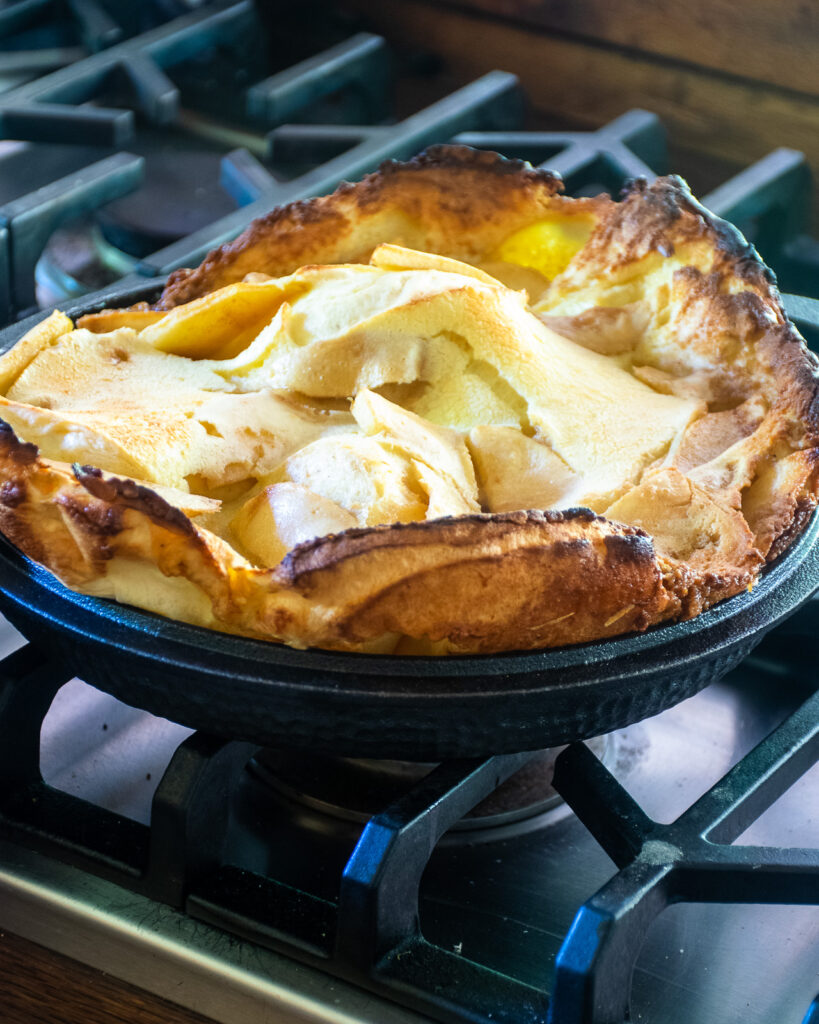 A puffed up apple Dutch baby in a cast iron skillet on a stovetop.