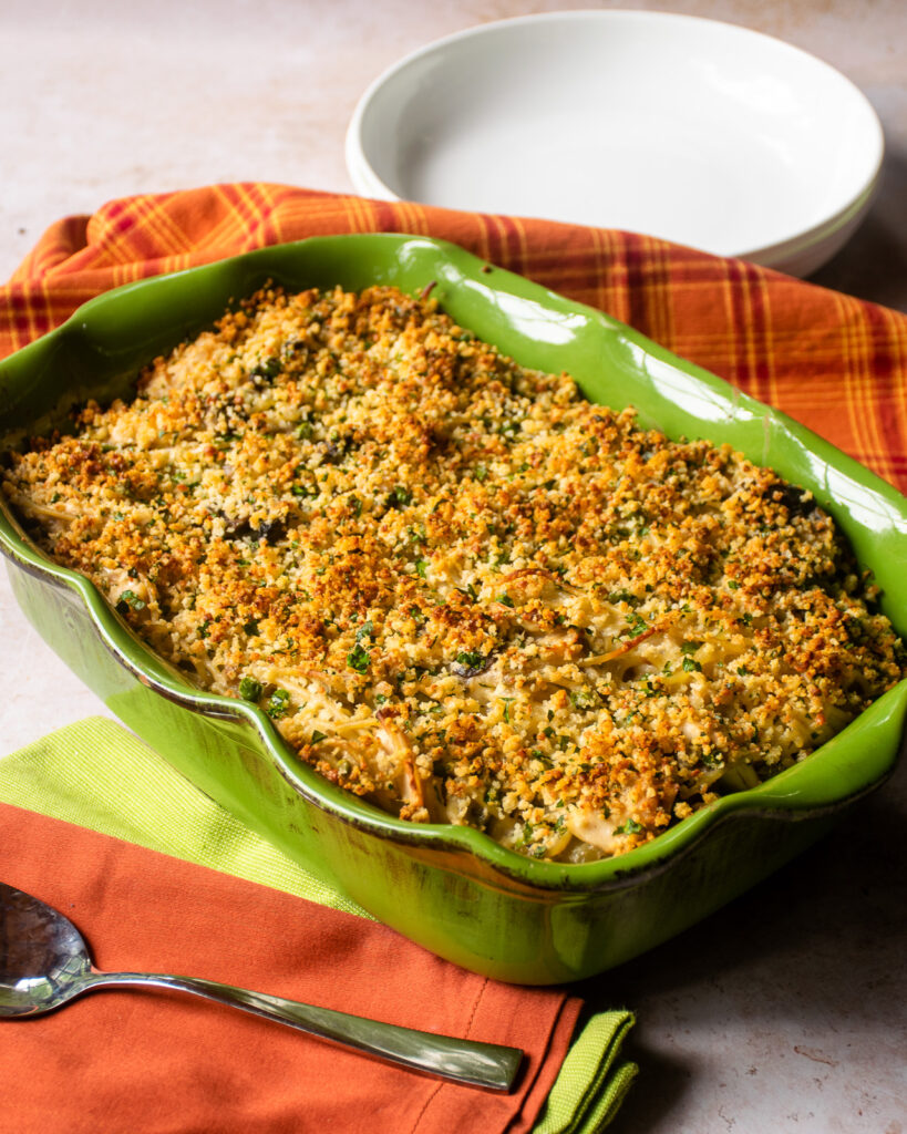 Turkey tetrazzini in a green scalloped casserole with orange and green napkins and a serving spoon.