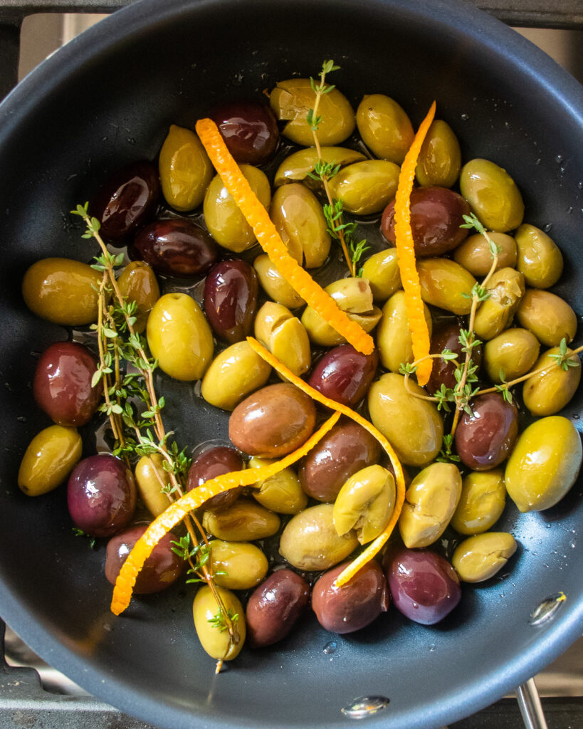 Looking straight down into a non-stick skillet with olives, orange peel and fresh thyme.