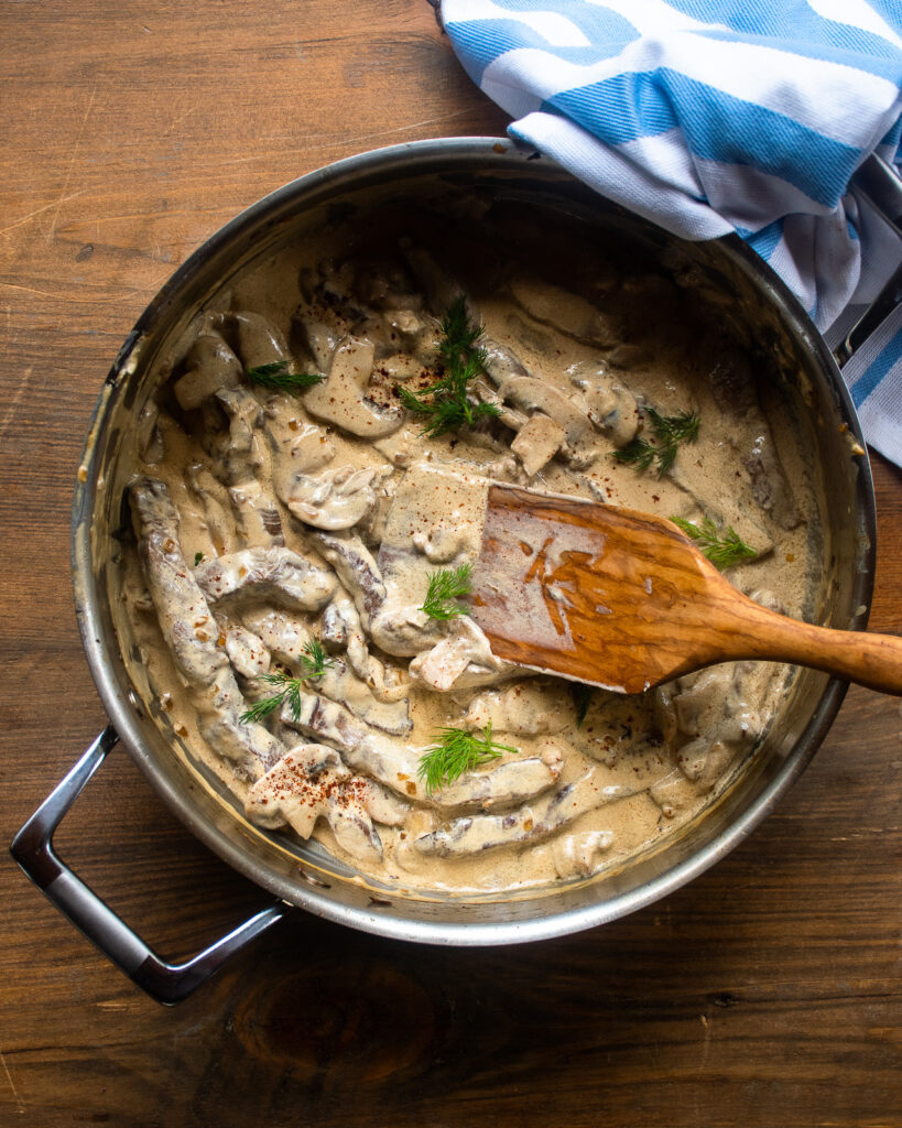 Beef stroganoff in a sauté pan with a wooden spoon sticking out of the pan.