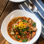 A white bowl of lentil soup with a spoon and napkin on a wooden table.