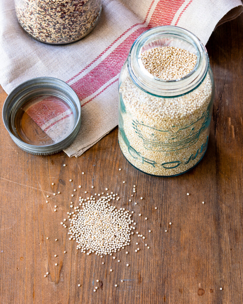 Looking down on a jar of white quinoa with the lid off and a pile of quinoa in front of it.