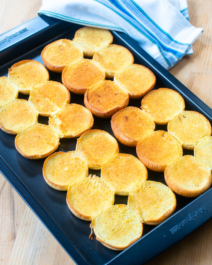 A baking sheet with 24 cut buns toasted on it.