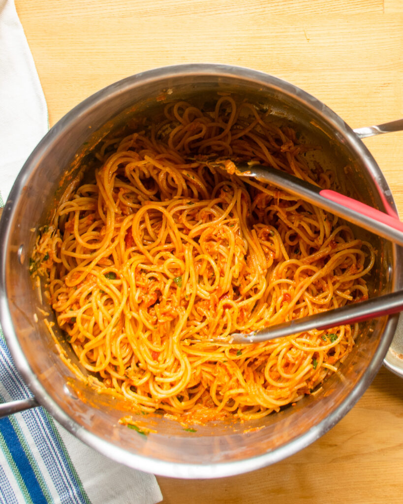 Looking down into a stockpot with spaghetti marinara inside and tongs sticking out.