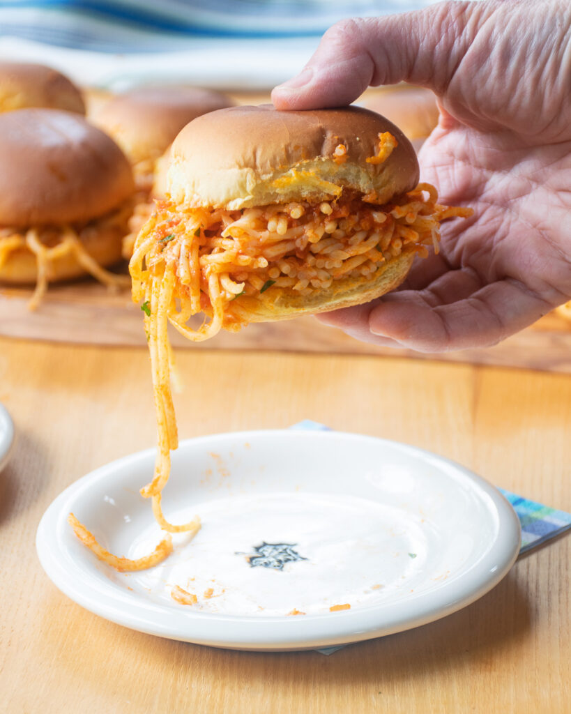 A hand lifting a spaghetti slider off a plate with more sliders in the background.